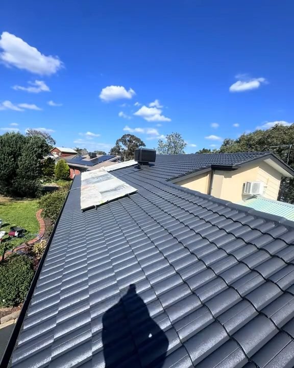 The same roof restored by ZX: dark coated tiles under a blue sky