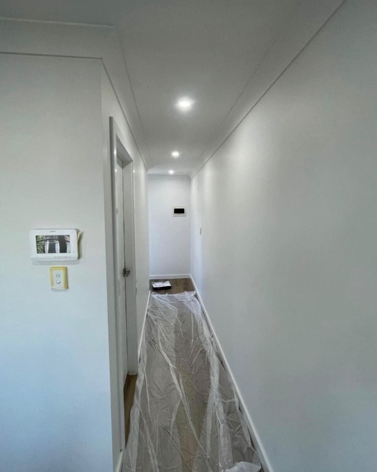 A freshly painted hallway: white walls, ceiling, doors and trims, the floor still covered